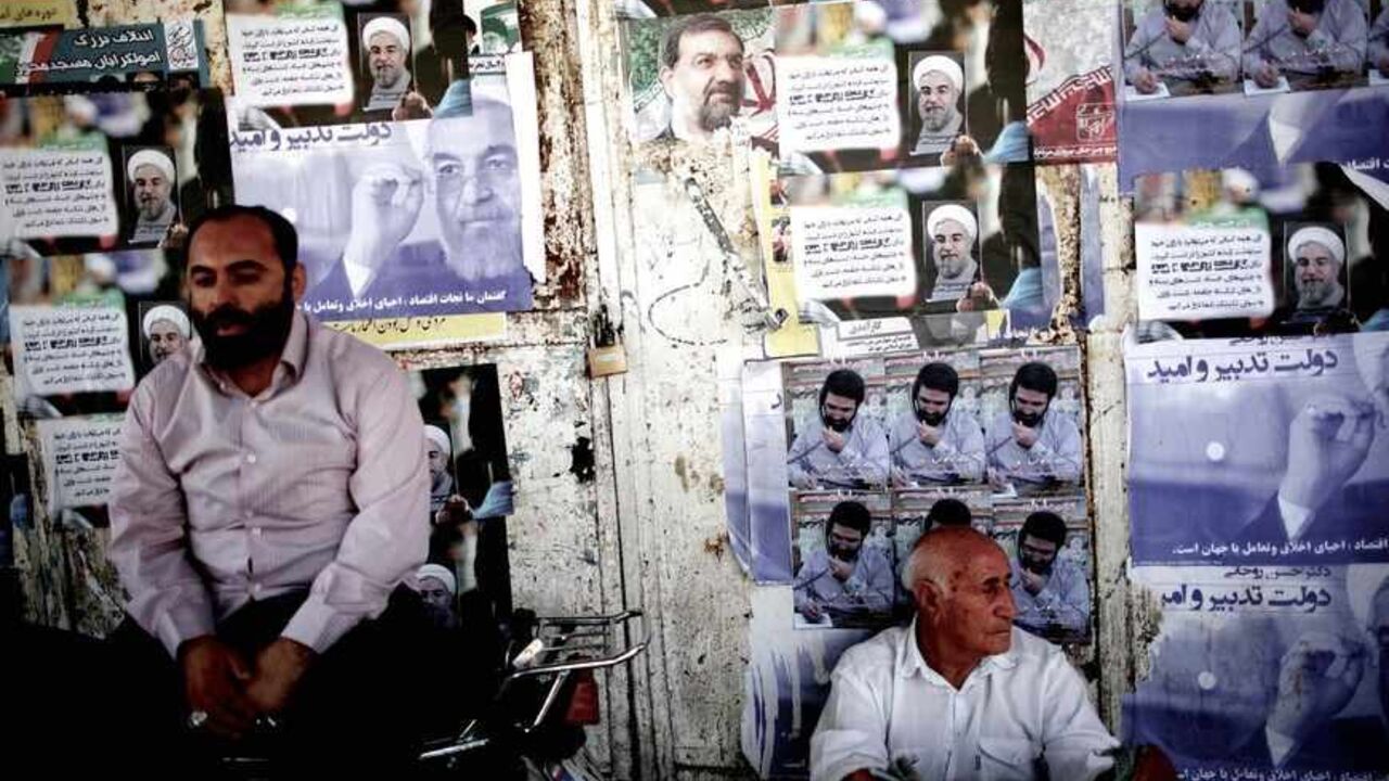 Nic6223153 Iranians sit next to electoral posters of Hassan Rohani (L) and Mohsen Rezai (C) in the religious city of Qom some 130 kilometres south of the capital on June 9, 2013. Iran elects on June 14 a successor to President Mahmoud Ahmadinejad, whose eight years in office have been marked by stiff Western sanctions over Tehran's controversial nuclear drive and the economic turmoil they have caused. AFP PHOTO/BEHROUZ MEHRI (Photo credit should read BEHROUZ MEHRI/AFP/Getty Images)