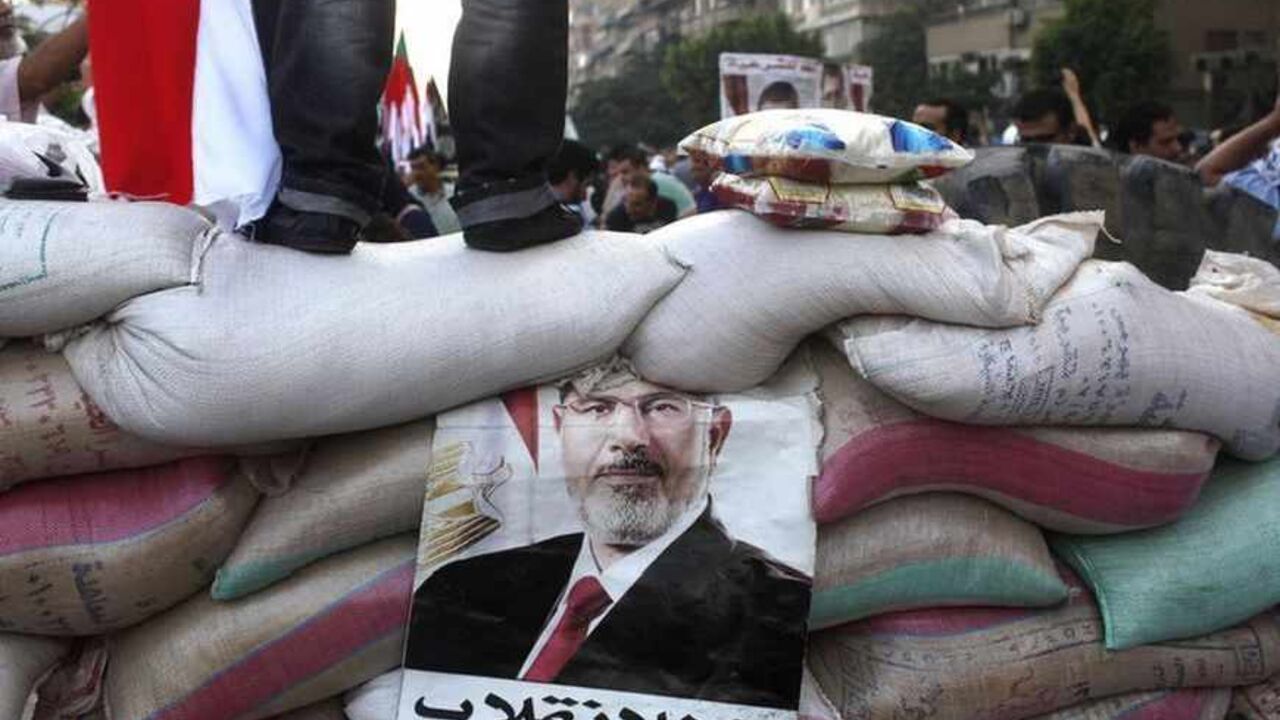 A poster of deposed Egyptian President Mursi is seen on a barrier made by members of the Muslim Brotherhood and Musi supporters to protect the sit-in area of Rab'a al- Adawiya Square, where they are camping A poster of deposed Egyptian President Mohamed Mursi is seen on a make-shift barrier of sand bags made by members of the Muslim Brotherhood and Musi supporters to protect the sit-in area of Rab'a al- Adawiya Square, where they are camping, on the first day of the Eid al-Fitr holiday after the end of the fasting month of Ramadan, in Cairo August 8, 2013. Islamist supporters of Mursi began marching to demand his restoration on Thursday after the military-led authorities that removed him held off from carrying