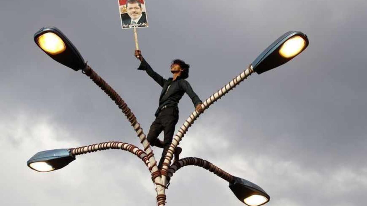 A supporter of deposed Egyptian President Mohamed Mursi holds up his photo while standing at the top of lamp posts during a march to show solidarity with his supporters in Egypt, in Sanaa A supporter of deposed Egyptian President Mohamed Mursi holds up his photo while standing at the top of lamp posts during a march to show solidarity with his supporters in Egypt, in Sanaa August 15, 2013. The poster reads "We are all with legitimacy". REUTERS/Mohamed al-Sayaghi (YEMEN - Tags: TPX IMAGES OF THE DAY CIVIL UNREST POLITICS) - RTX12MHB