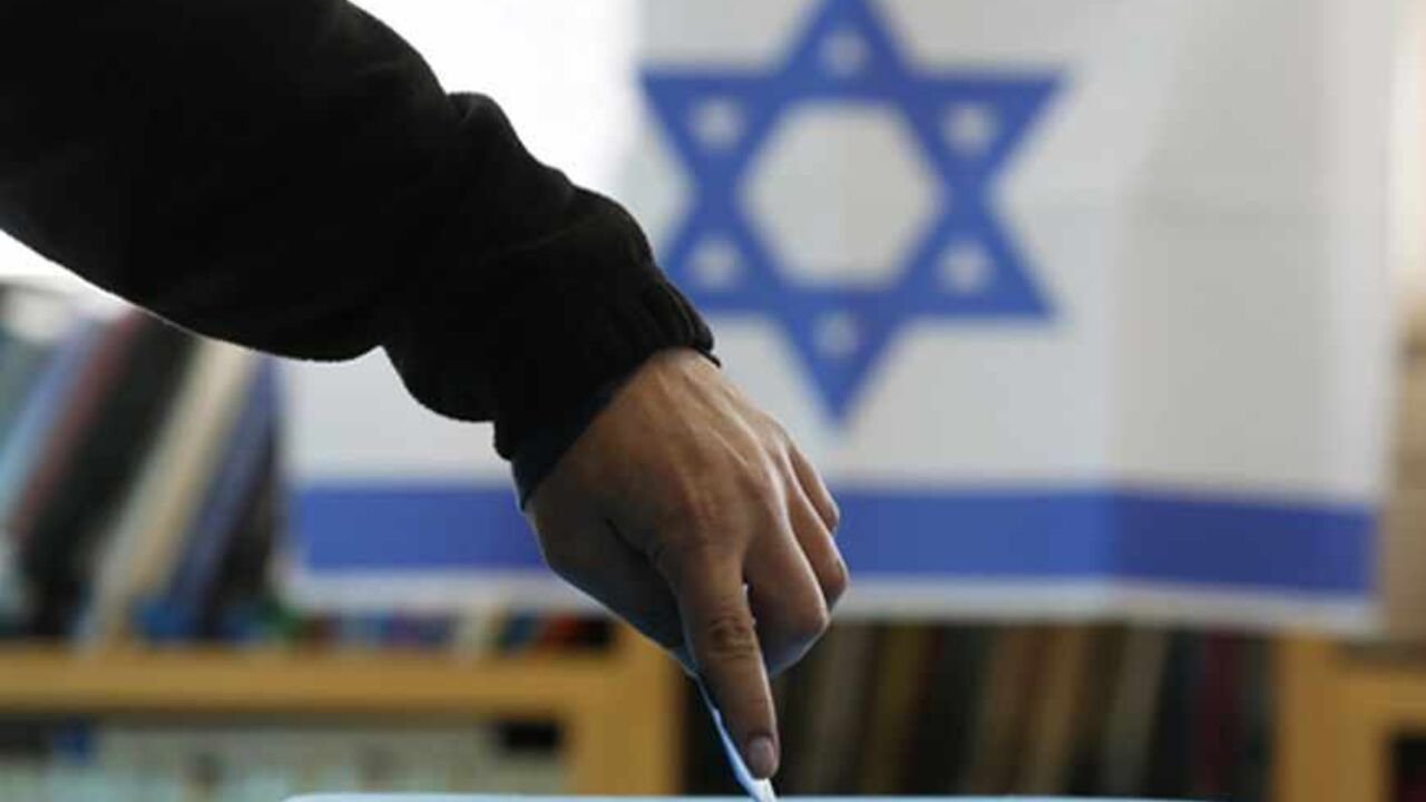 An Israeli flag is seen in the background as a man casts his ballot for the parliamentary election at a polling in the West Bank Jewish settlement of Ofra, north of Ramallah January 22, 2013. Israelis voted on Tuesday in an election that is expected to see Prime Minister Benjamin Netanyahu win a third term in office, pushing the Jewish state further to the right, away from peace with the Palestinians and towards a showdown with Iran. REUTERS/Baz Ratner (WEST BANK - Tags: POLITICS ELECTIONS TPX IMAGES OF THE