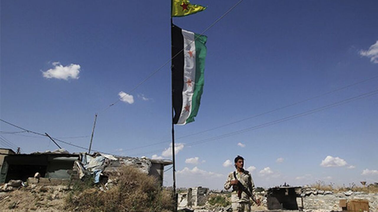 SYRIA-CRISIS/ A Free Syrian Army fighter carrying his weapon, walks along a street as Syrian opposition (bottom) and Popular Protection Units (YPG) flags flutter, in Aleppo's Sheikh Maqsoud neighbourhood, June 7, 2013. Kurdish fighters from the Popular Protection Units (YPG) joined the Free Syrian Army fighters to fight against forces loyal to Syria's President Bashar al-Assad. Picture taken June 7, 2013. REUTERS/Muzaffar Salman (SYRIA - Tags: CIVIL UNREST POLITICS CONFLICT) - RTX10USV