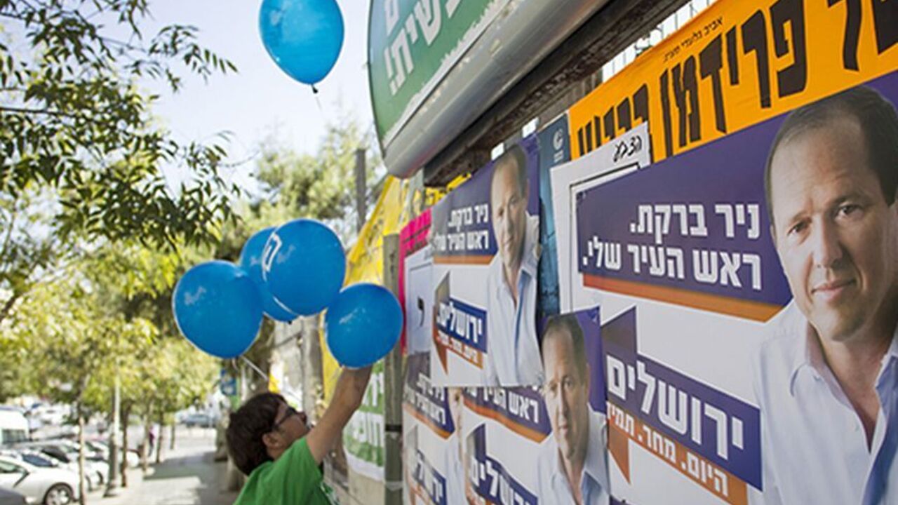ISRAEL/ A supporter of the left wing Meretz party campaigning for municipal elections hangs balloons next to campaign posters of Jerusalem Mayor Nir Barkat in Jerusalem October 22, 2013. REUTERS/Baz Ratner (JERUSALEM - Tags: POLITICS ELECTIONS) - RTX14JPY