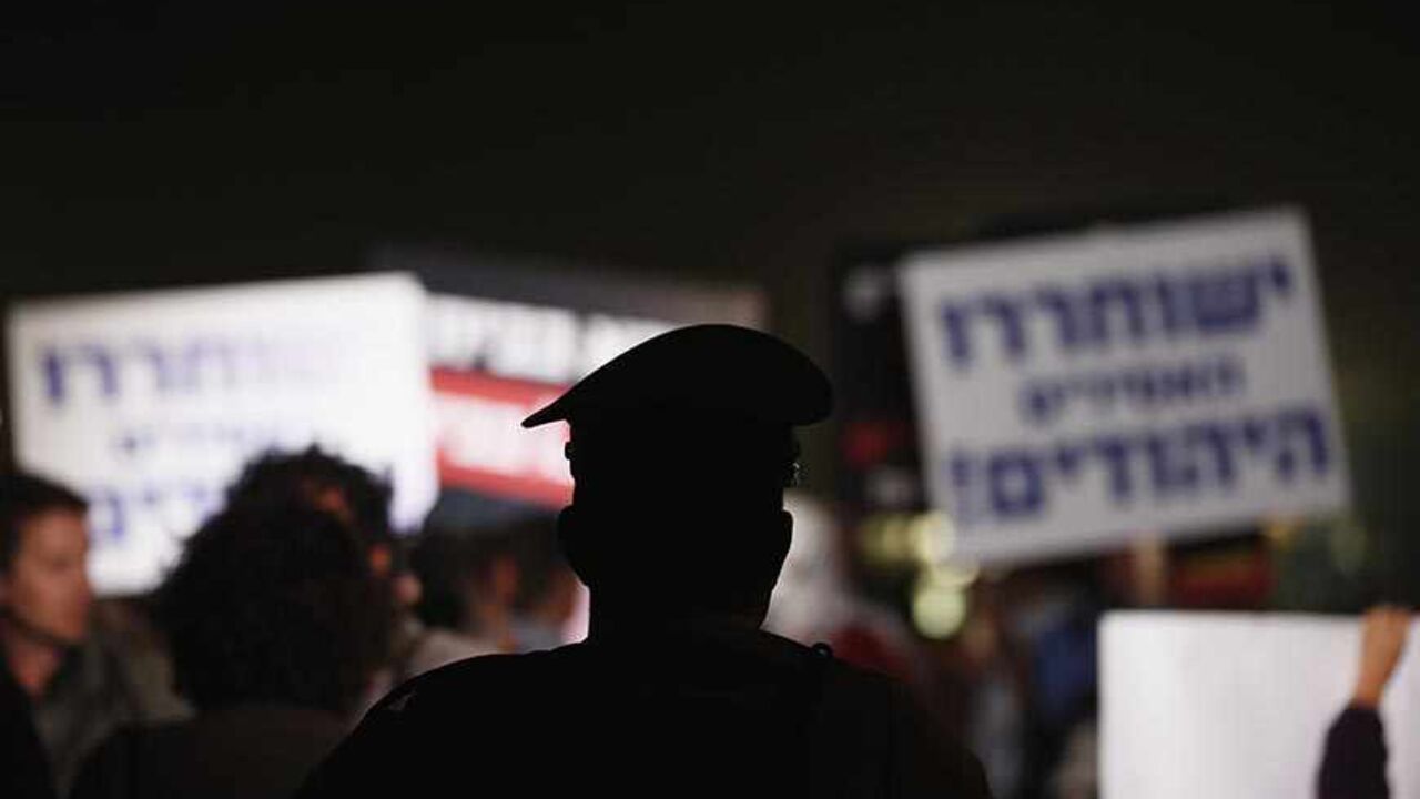 PALESTINIANS-ISRAEL/ A police officer watches Israeli protesters take part in a rally against the release of Palestinian prisoners in Israeli jails outside Ofer prison near the West Bank city of Ramallah, October 29, 2013. Israel is to release 26 Palestinian prisoners in a second stage of a deal brokered by the United States in July that brought a resumption of peace talks. REUTERS/Darren Whiteside (ISRAEL - Tags: CIVIL UNREST POLITICS RELIGION) - RTX14SWY