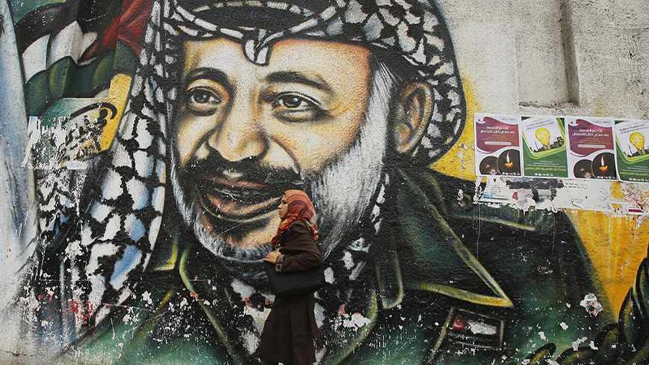 PALESTINIANS-ARAFAT/SWISS A Palestinian student walks past a mural depicting late Palestinian leader Yasser Arafat in Gaza City November 7, 2013. Swiss scientists who conducted tests on the remains of Palestinian leader Yasser Arafat, whose widow Suha says he was poisoned by radioactive polonium, will give a news conference on Thursday on their findings. REUTERS/Suhaib Salem (GAZA - Tags: POLITICS CRIME LAW SOCIETY) - RTX153OJ