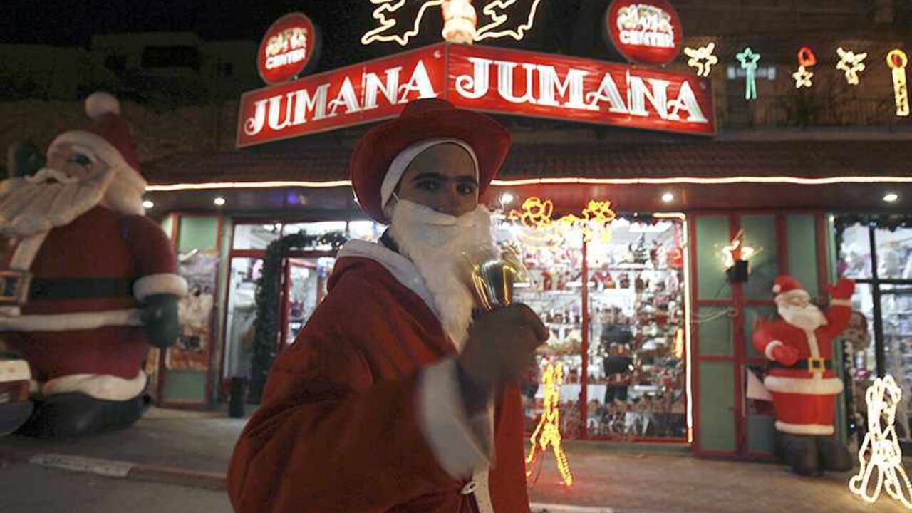 PALESTINIANS/ A Palestinian man dressed as Santa Claus rings a bell as he stands outside a shop in the West Bank city of Bethlehem December 23, 2007. Bethlehem is about to celebrate its most peaceful -- and profitable -- Christmas since 2000. Tourist levels are the best in seven years, with more than 60,000 people visiting last month compared to about 20,000 a year ago. REUTERS/Ammar Awad (WEST BANK) - RTX4Z3F