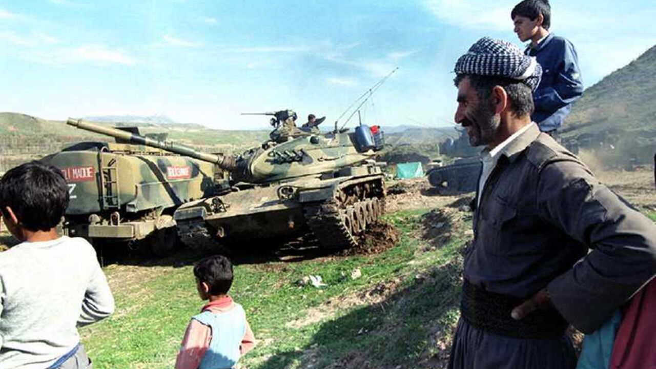 An Iraqi Kurdish pashmarga (fighter) and a group of children watch Turkish tank movement near a small village in the mountains in Northern Iraq March 22. Thirty-five thousand Turkish soldiers backed by tanks and air power entered into northern Iraq to launch an offensive against PKK Kurdish guerrillas on March 20 - RTXG5C1