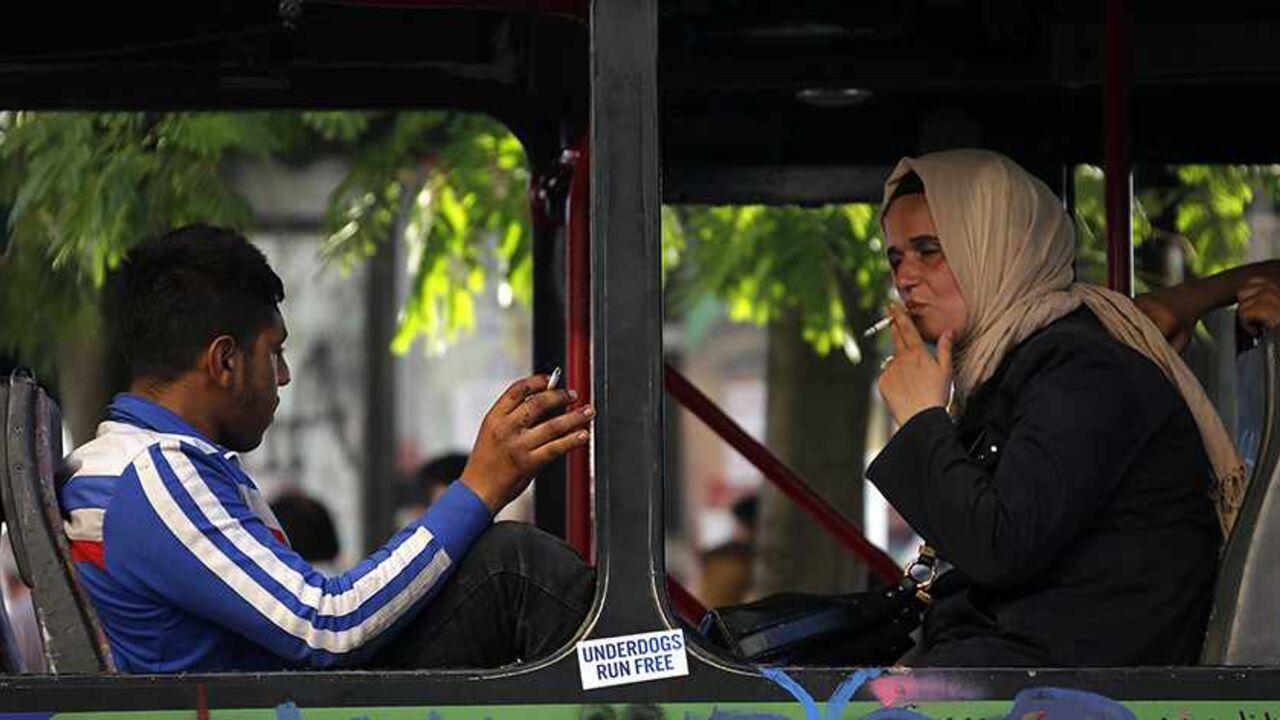 TURKEY-PROTESTS/ A woman wearing a traditional head-scarf smokes a cigarette inside a damaged bus used by anti-government protesters as a barricade in Istanbul's Taksim square June 10, 2013. REUTERS/Yannis Behrakis (TURKEY - Tags: CIVIL UNREST POLITICS) - RTX10IVP