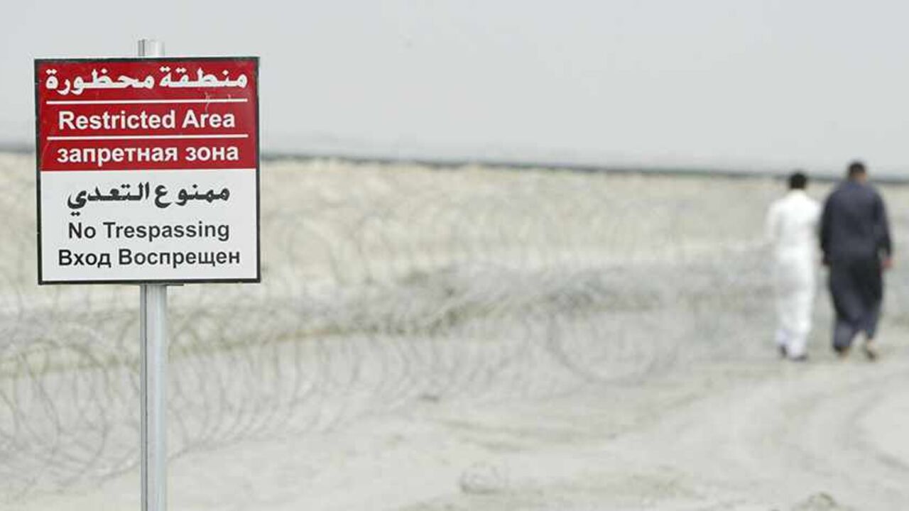 IRAQ-OIL/TRIBES Men walk past a sign in al-Toraba area near an oilfield of West Qurna-2 in Basra, 420 km (261 miles) southeast of Baghdad, October 26, 2013. After struggling for decades from sanctions and wars, most recently the U.S.-led invasion from 2003-2011, expectations run high among the 150,000 tribesmen living on West Qurna-2, the world's second-largest undeveloped oilfield. Their sheer number leaves Lukoil with a far tougher challenge than rival firms operating the huge but sparsely populated fields nearby. Pictur