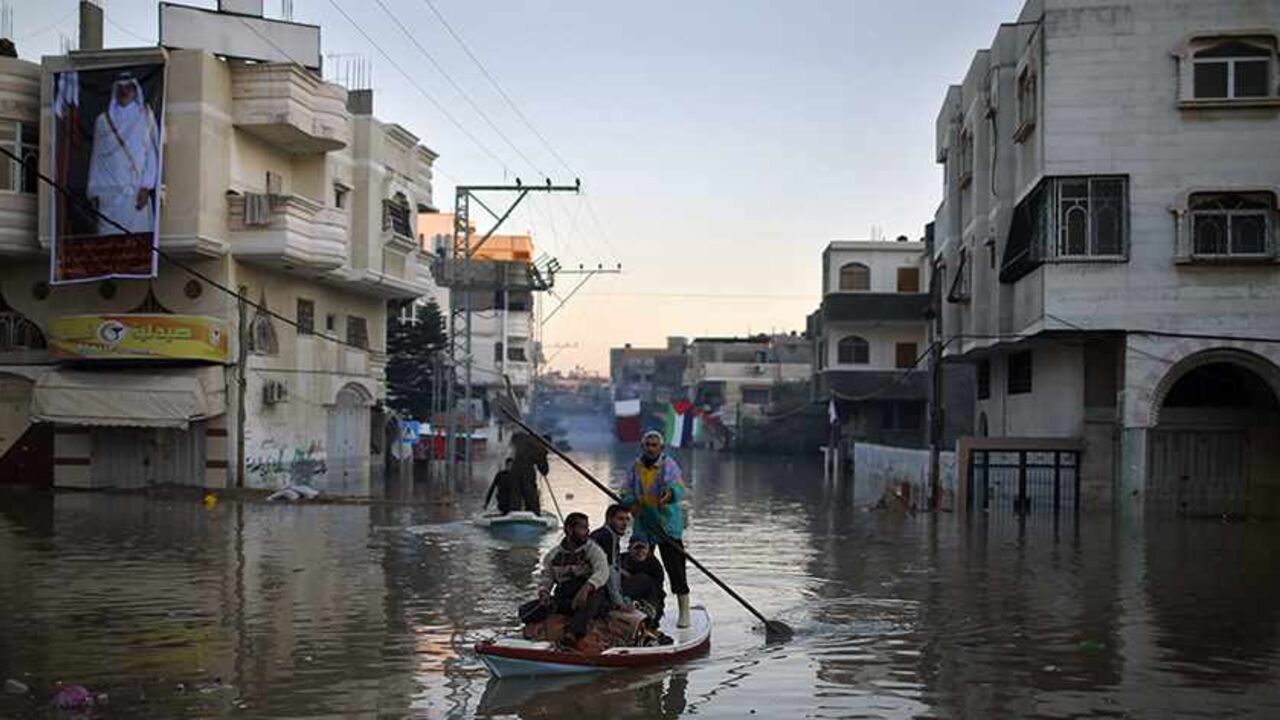 PALESTINIANS-GAZA/FUEL Palestinian civil defence volunteers paddle a boat to evacuate people from their houses that are flooded with rainwater as a poster depicting Qatar's Emir Sheikh Tamim bin Hamad is seen on a building, in the northern Gaza Strip December 16, 2013. Israel allowed the entry of 450,000 litres of fuel, paid for by Qatar, into the Gaza Strip on Sunday to enable the Palestinian territory's sole power plant to resume operations. Qatar answered an appeal by Gaza's government, led by the Islamist Hamas group, after f