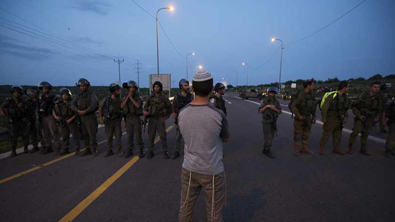 A Jewish settler stands in front of Israeli soldiers during a protest at the site of a stabbing attack by a Palestinian, at Tapuach junction, near the West Bank city of Nablus April 30, 2013. A Palestinian man stabbed and shot dead an Israeli settler in the occupied West Bank on Tuesday, the Israeli ambulance service and police said. REUTERS/Ronen Zvulun (WEST BANK - Tags: POLITICS CIVIL UNREST TPX IMAGES OF THE DAY) - RTXZ5CW