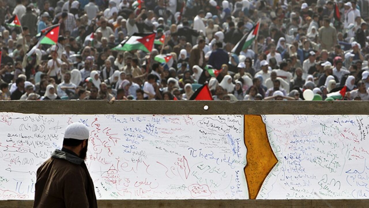 JORDAN/ A Palestinian refugee walks past a banner painted with the map of Palestine during a demonstration to mark the 63rd anniversary of "Nakba", Arabic for "Catastrophe", the term used to mark the events leading to Israel's founding in 1948, in Shouneh west of Amman May 13, 2011. Nearly 5,000 Jordanians gathered in the Jordan Valley near the Israeli border to demand an end to the occupation of Palestinian territories. REUTERS/Muhammad Hamed (JORDAN - Tags: POLITICS CIVIL UNREST ANNIVERSARY) - RTR2MDQS