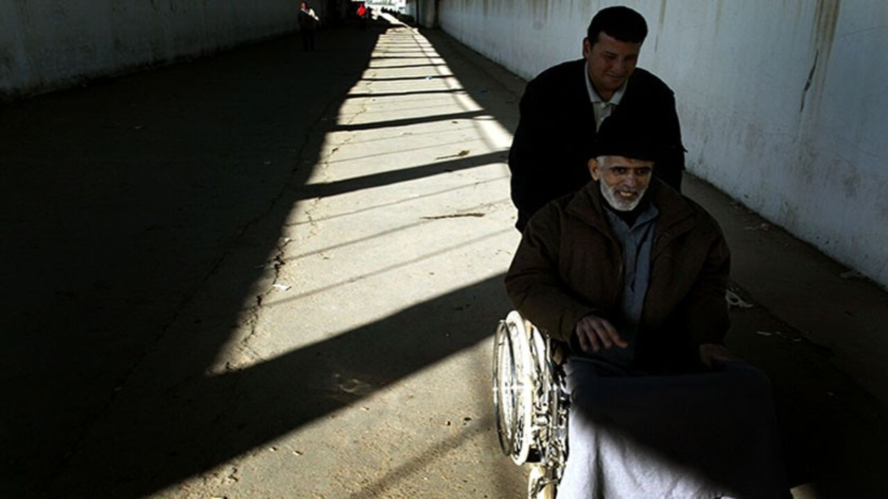MIDEAST A PORTER PUSHES AN ELDERLY PALESTINIAN CANCER PATIENT THROUGH THE EREZ CROSSING BETWEEN THE GAZA STRIP AND ISRAEL. A porter pushes an elderly Palestinian cancer patient through the Erez crossing between the Gaza Strip and Israel March 21, 2004. Palestinian doctors complain Israel has stopped allowing ambulances to bring patients into Israel from Gaza, forcing the sick to cross unaided through the heavily guarded checkpoint. REUTERS/Goran Tomasevic - RTRFRM5