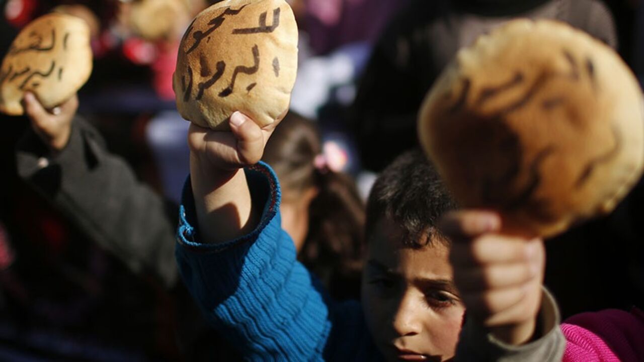 PALESTINIANS/ Palestinian children hold bread as they take part in a rally to show solidarity with Palestinian refugees in Syria's main refugee camp Yarmouk, in Gaza City January 16, 2014. The Arabic words on the bread read: "No to starving Yarmouk" REUTERS/Mohammed Salem (GAZA - Tags: POLITICS CIVIL UNREST) - RTX17G3P