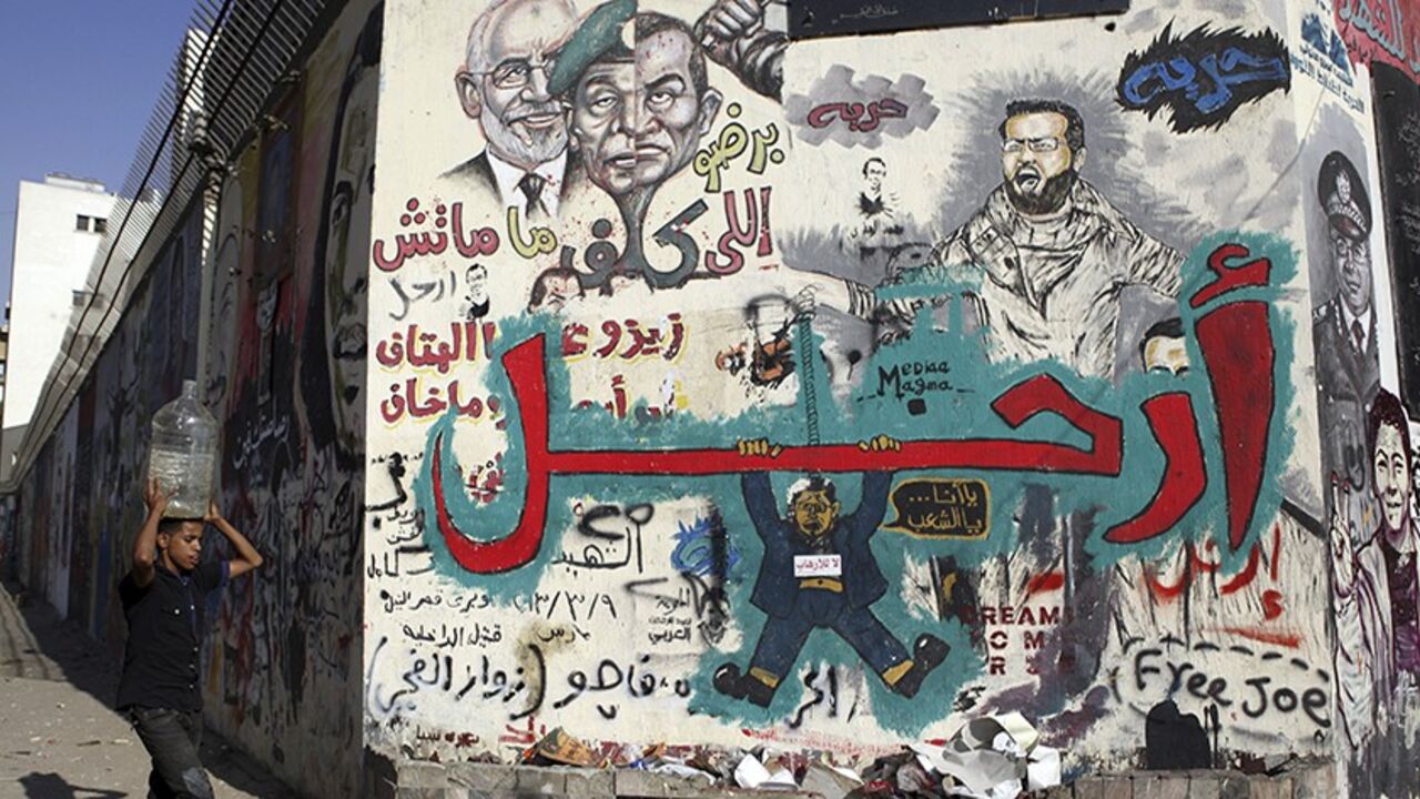 EGYPT-PROTESTS/ A man carrying a water container on his head walks in front of a wall filled with graffiti depicting deposed Egyptian President Mohamed Mursi with a message reading "Leave", at Tahrir Square in Cairo July 14, 2013. Egypt's interim prime minister filled senior posts on Sunday in a cabinet that will lead the country under an army-backed "road map" to restore civilian rule following overthrow of Mursi. REUTERS/Amr Abdallah Dalsh (EGYPT - Tags: POLITICS CIVIL UNREST) - RTX11MPT
