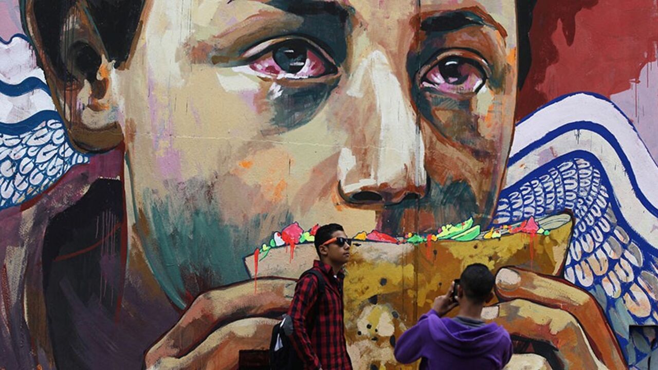 EGYPT-FOREX/ Youths take photos in front of graffiti depicting poverty and homelessness in downtown Cairo December 5, 2013. The Egyptian pound was steady at official rates on Thursday, the central bank said, and slightly stronger in the black market, two sources said - a day after the bank's governor said that parallel market for dollars would "not last long". REUTERS/Amr Abdallah Dalsh (EGYPT - Tags: POLITICS SOCIETY BUSINESS TPX IMAGES OF THE DAY) - RTX164R2