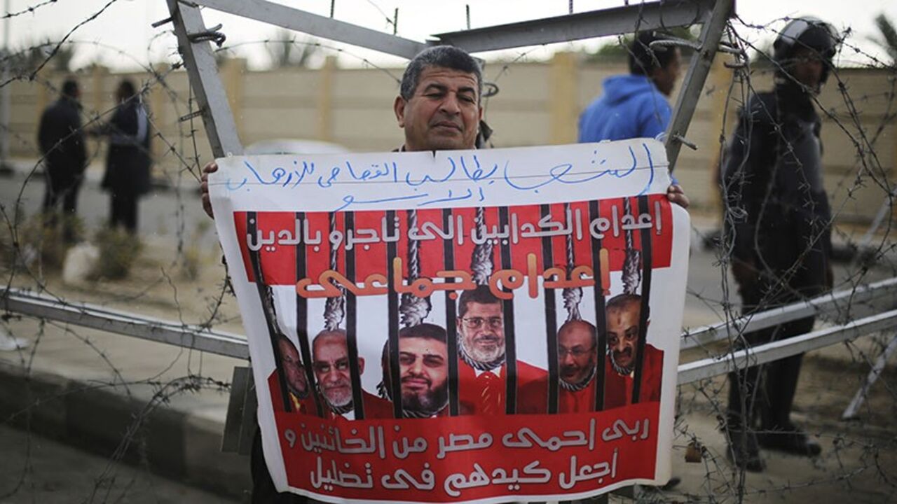 EGYPT-MURSI/ A supporter of Egypt's army chief Field Marshal Abdel Fattah al-Sisi rallies outside a police academy, where the trial of ousted Egyptian President Mohamed Mursi and members of the Muslim Brotherhood is due to take place, on the outskirts of Cairo, February 16, 2014. Mursi appeared in court on Sunday on charges of conspiring with foreign groups to commit terrorist acts in Egypt, in a further escalation of the crackdown against his Muslim Brotherhood. The poster, showing Mursi (C) and Muslim Brotherhood lead
