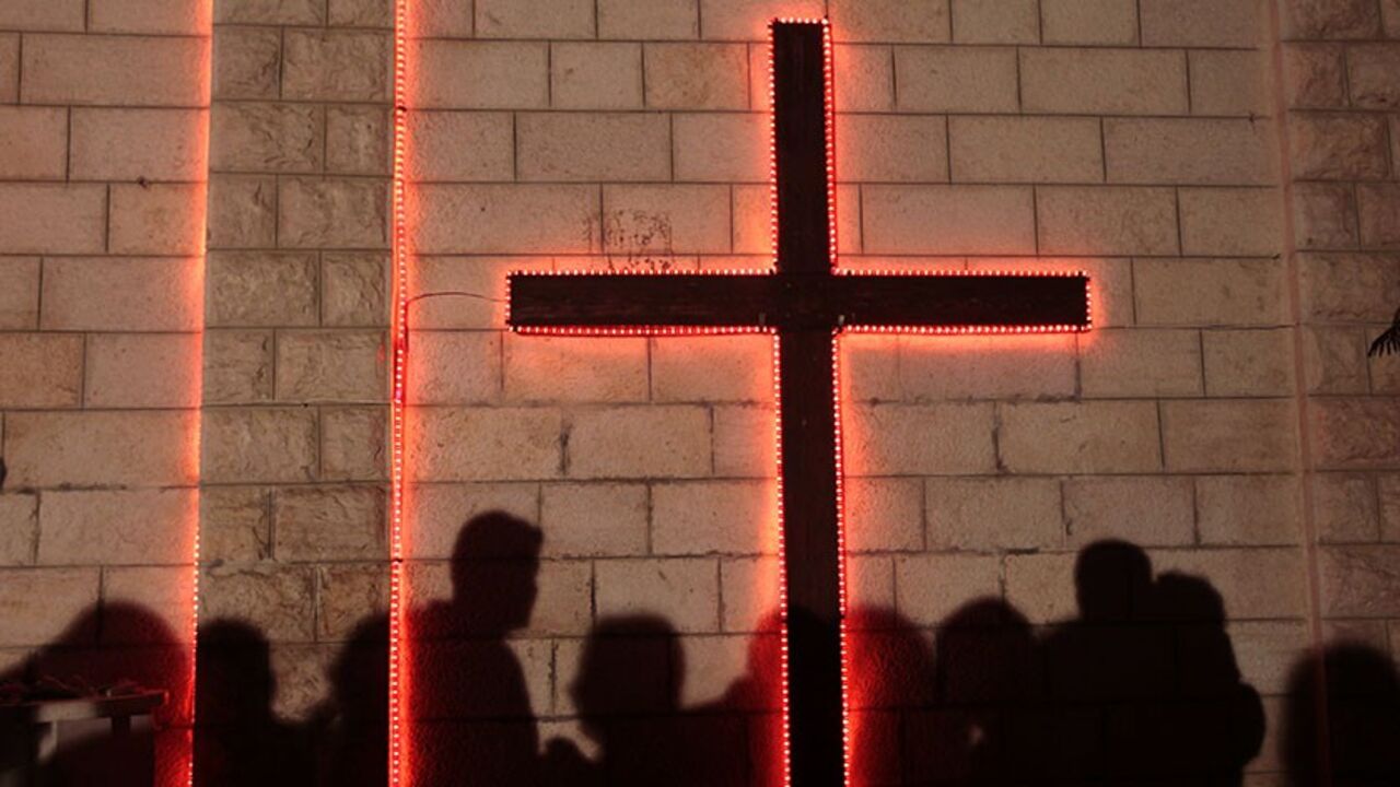 PALESTINIANS-ISRAEL/ Shadows of Palestinians are cast on a wall with a cross at Gaza's Der Latin church on Christmas Eve December 24, 2009 as they wait for the Christmas mass. Less than 100 Gazans gathered in the church to take part in the Christmas celebrations. REUTERS/Yannis Behrakis (GAZA - Tags: RELIGION POLITICS SOCIETY) - RTR28C3I