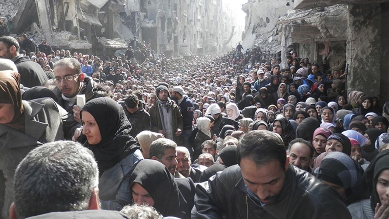 SYRIA-CRISIS/AID Residents wait to receive food aid distributed by the U.N. Relief and Works Agency (UNRWA) at the besieged al-Yarmouk camp, south of Damascus on January 31, 2014, in this handout picture made available to Reuters February 26, 2014. World powers have passed a landmark Security Council resolution demanding an end to restrictions on humanitarian operations in Syria, but aid workers doubt it has the punch to make Damascus grant access and let stuck convoys deliver vital supplies. The resolution called for the i