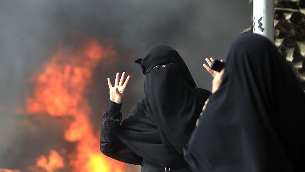 EGYPT/ A student and supporter of the Muslim Brotherhood and ousted Egyptian President Mohamed Mursi gestures with the sign "Rabaa", or "Four", in front of a burning car during a protest inside Cairo University, in Cairo, March 9, 2014. REUTERS/Mohamed Abd El Ghany (EGYPT - Tags: POLITICS CIVIL UNREST EDUCATION) - RTR3GBFP