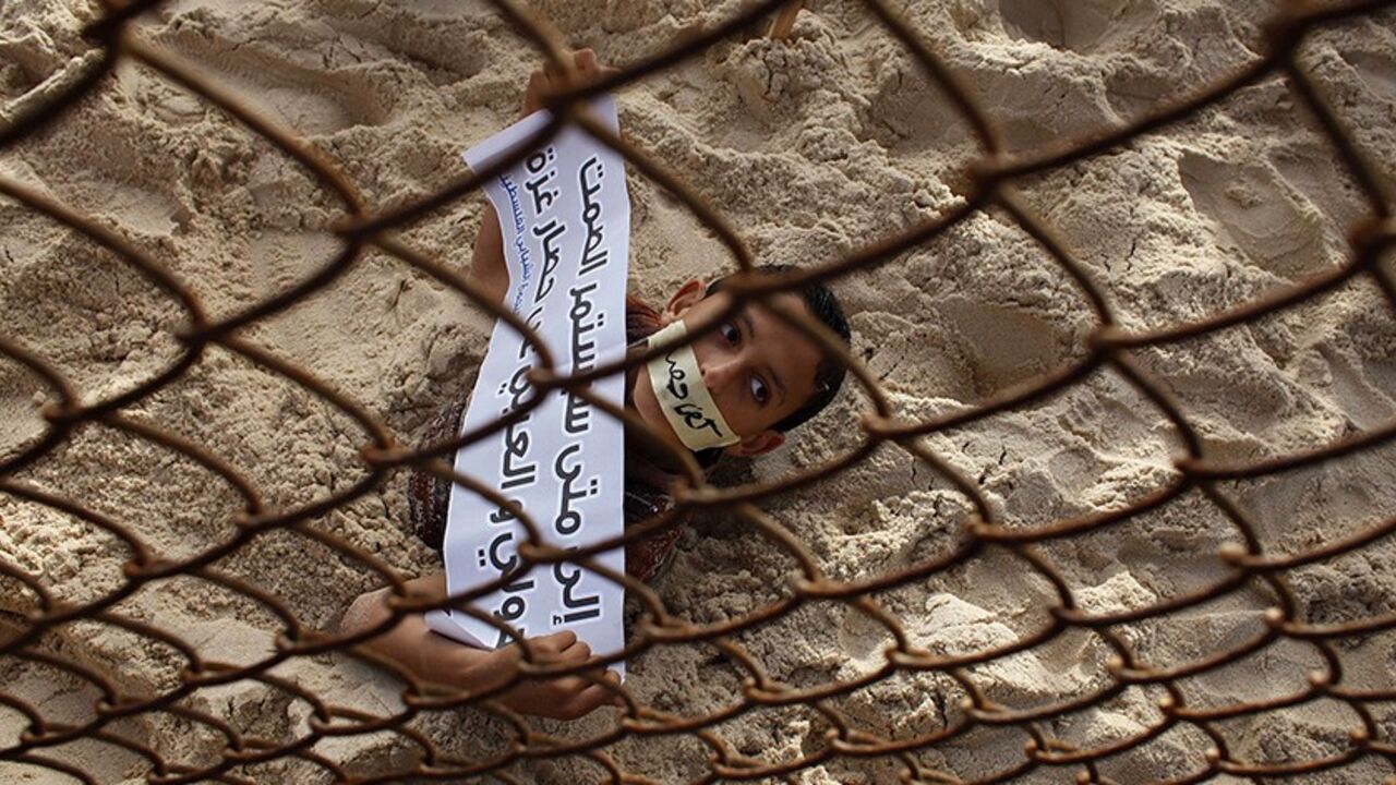 PALESTINIANS-ISRAEL/ A Palestinian boy takes part in a protest against the blockade on Gaza, at the border between Egypt and Gaza Strip March 7, 2014. An Egyptian-Israeli blockade on the Gaza Strip, run by the Hamas Islamist movement, has left industry and construction gasping for resources, pushing unemployment to dizzying heights and deepening suffering for impoverished residents. The sign reads "How long will the international and Arab silence on Gaza blockade continue". REUTERS/Ibraheem Abu Mustafa (GAZA - Tags: POLITICS CI