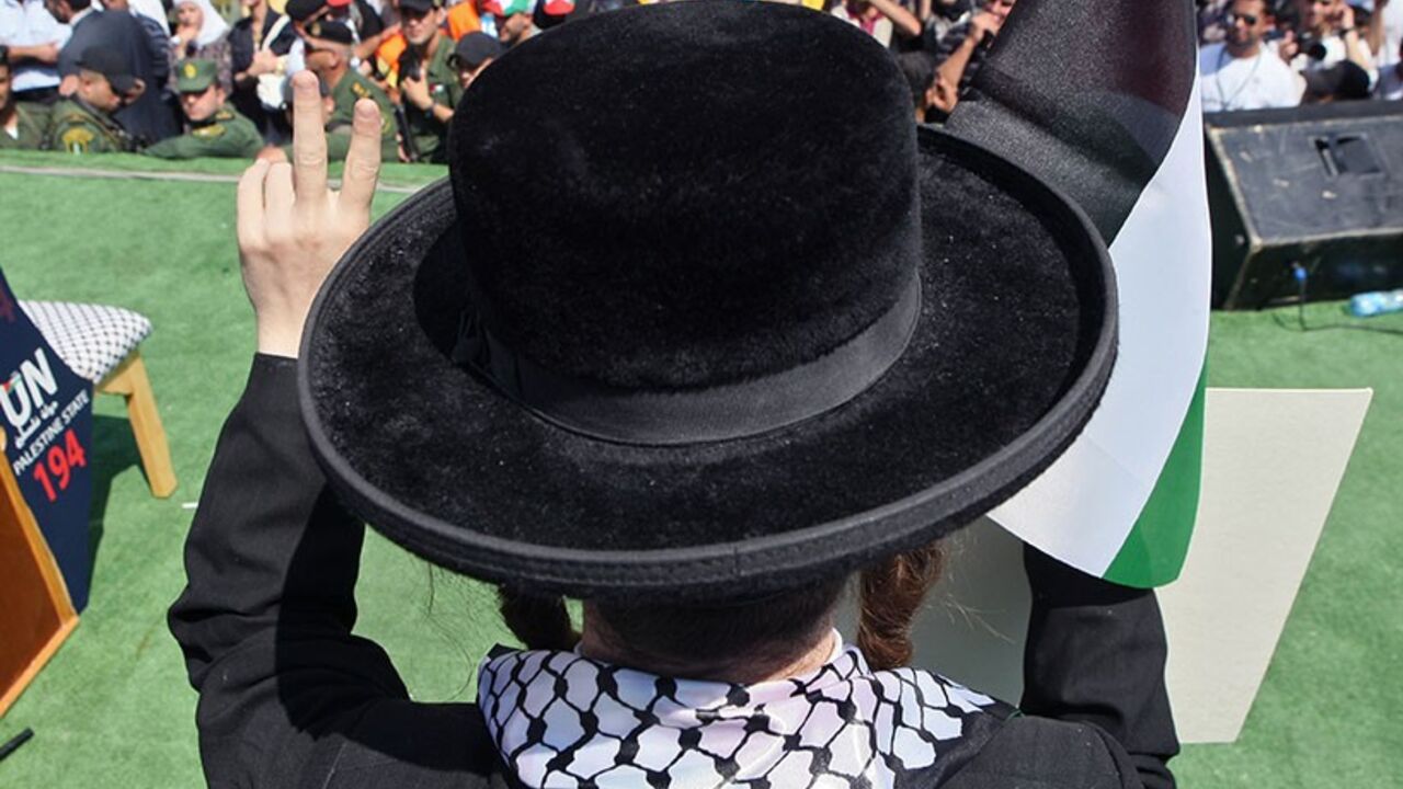 DV1045345 A member of Neturei Karta, a small faction of ultra-Orthodox Jews who oppose Israel's existence, waves a Palestinian flag to express support for the Palestinian bid for statehood recognition at the United Nations as thousands of Palestinians attend a demonstration on September 21, 2011 in the West Bank city of Nablus. Palestinians are preparing to submit a formal request to become the 194th member of the United Nations when the General Assembly begins its meetings on September 20, despite US and Israeli opp