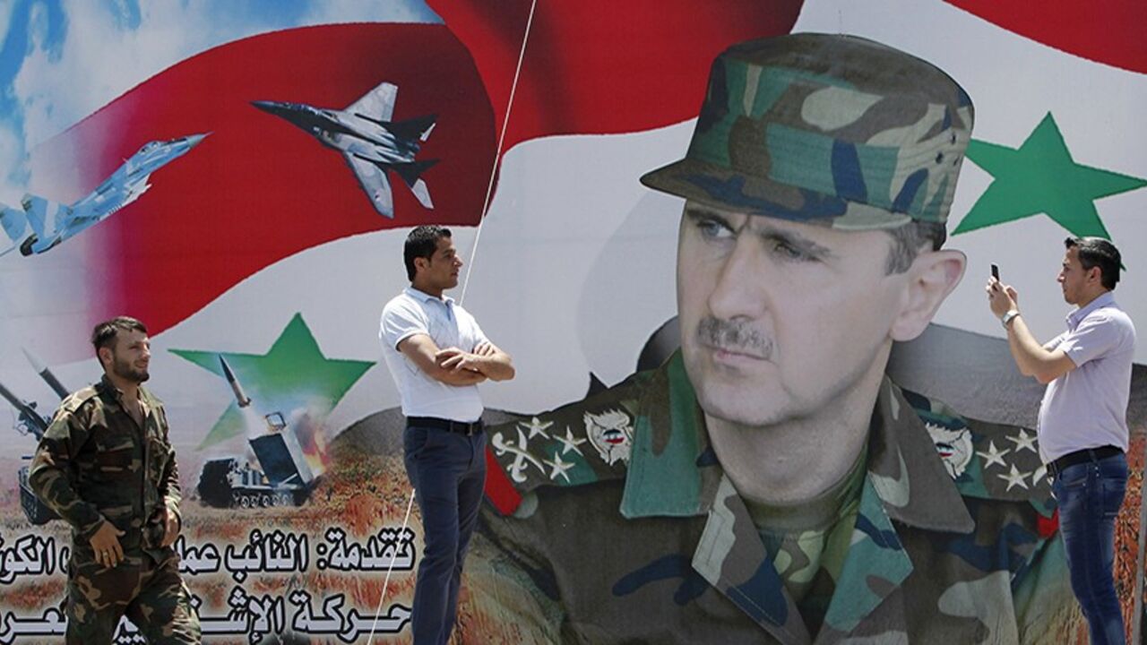 A man takes a photo of his friend in front of a poster of Syria's President Bashar al-Assad at Umayyad Square in Damascus May 16, 2014. Syria is holding a presidential election for June 3, preparing the ground for Assad to defy widespread opposition and extend his grip on power, days after he said the civil war was turning in his favour. Opponents have dismissed the vote as a farce.   REUTERS/Khaled al-Hariri (SYRIA - Tags: POLITICS ELECTIONS CIVIL UNREST CONFLICT) - RTR3PGCV