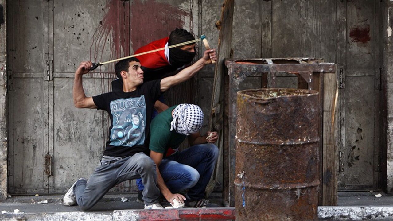 ISRAEL-PALESTINIAN/CLASHES/ A Palestinian protester uses a sling to hurl a stone at Israeli troops during clashes following a rally to show solidarity with Palestinian prisoners held in Israeli jails, in the West Bank city of Hebron May 16, 2014. Some 120 Palestinians jailed without trial in Israel have been on an open-ended hunger strike, eating only salt and drinking water, for the past 23 days to demand an end to so-called "administrative detention". REUTERS/Mussa Qawasma (WEST BANK - Tags: POLITICS CIVIL UNREST) - RTR3PIGO