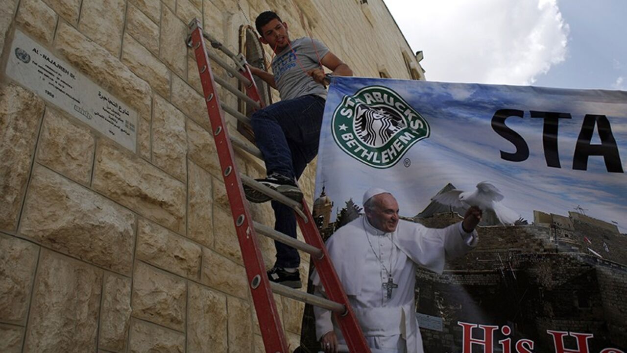 POPE-HOLYLAND/ A Palestinian hangs a poster of Pope Francis in the West Bank town of Bethlehem May 22, 2014. With a Rabbi and a Muslim leader in tow, Pope Francis makes his first visit to the Middle East on Saturday, a delicate mission to push his vision of inter-religious dialogue as a vehicle for peace in the region. He will visit Jordan, the Palestinian Territories and Israel during his May 24-26 trip. REUTERS/Mohamad Torokman (WEST BANK - Tags: RELIGION POLITICS) - RTR3QD6G
