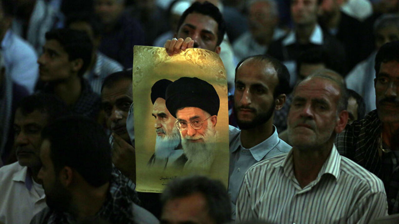 IRAN-POLITICS-ROUHANI-KHOMEINI-ANNIVERSARY An Iranian man holds a photo showing Iran's supreme leader Ayatollah Ali Khamenei, and Iran's late Ayatollah Ruhollah Khomeini, while listening to Iran's President Hassan Rouhani delivering a speech on the eve of the 25th anniversary of the death of Islamic revolutionary leader Khomeini, at Khomeini's mausoleum in a suburb of Tehran on June 3, 2014. AFP PHOTO / ATTA KENARE (Photo credit should read ATTA KENARE/AFP/Getty Images)