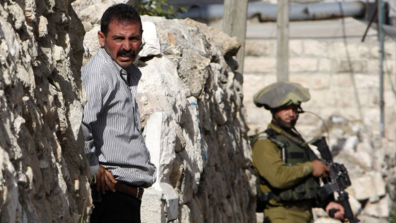 A Palestinian man stands outside his house as an Israeli soldier takes part in an operation to locate three Israeli teens in Hebron A Palestinian man stands outside his house as an Israeli soldier takes part in an operation to locate three Israeli teens in the West Bank City of Hebron June 19, 2014. Israeli forces traded gunfire with Palestinians on Thursday, the military said, in the fiercest street battles in the occupied West Bank since a search began for three Israeli teenagers missing for a week. REUTERS/Mussa Qawasma (WEST BANK - Tags: POLITICS MILITARY) - RTR3UOFG