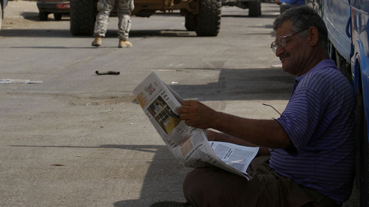 A motorist reads newspaper on street near U.S. patrol passing by in Baghdad A motorist reads a newspaper on a street near a U.S. patrol passing by in Baghdad September 4, 2008. REUTERS/Mohammed Ameen (IRAQ) - RTX8E9D