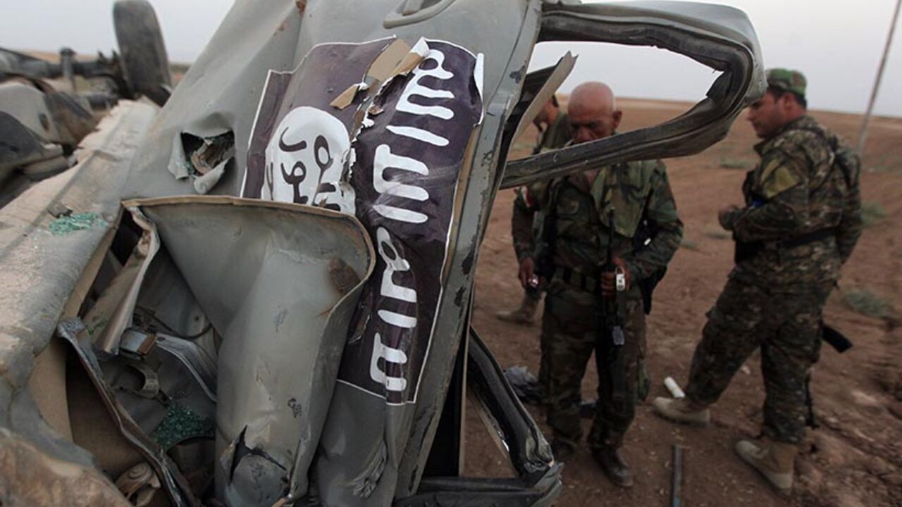 IRAQ-UNREST Peshmerga fighters inspect the remains of a car, bearing an image of the trademark jihadist flag, which belonged to Islamic State (IS) militants after it was targeted by an American air strike in the village of Baqufa, north of Mosul, on August 18,2014. Kurdish peshmerga fighters backed by federal forces and US warplanes pressed a counter-offensive Monday against jihadists after retaking Iraq's largest dam, as the United States and Britain stepped up their military involvement. AFP PHOTO/AHMAD AL-RUBAYE