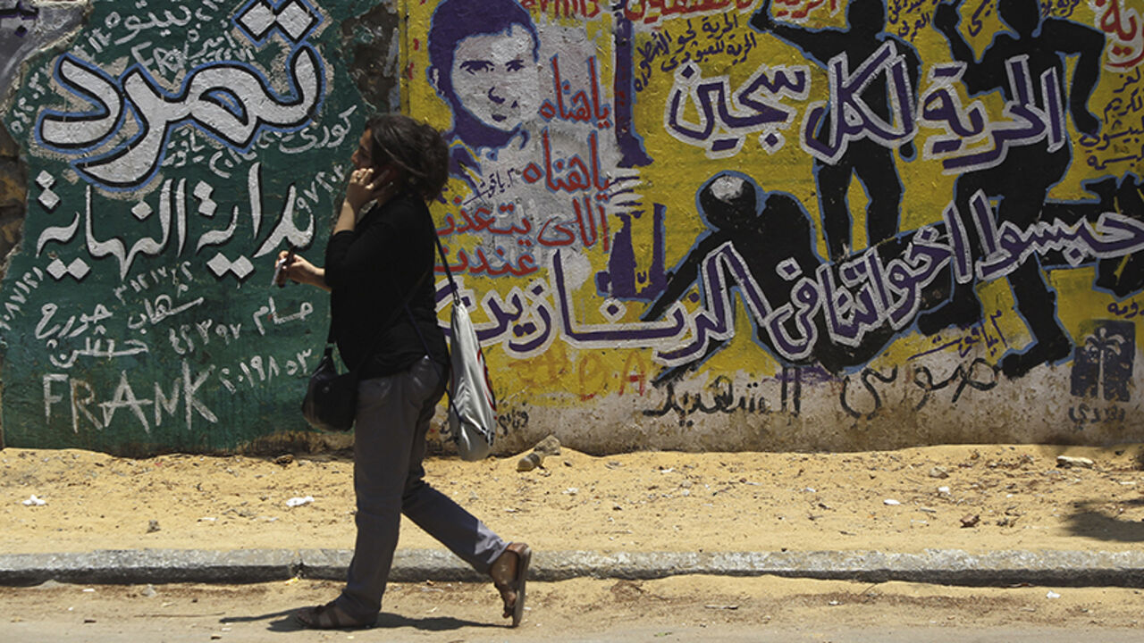 EGYPT- A woman walks past graffiti depicting riot police near Tahrir Square in Cairo June 23, 2013. The "Rebel!" alliance is campaigning to force President Mohamed Mursi to resign. Mursi's opponents say they have gathered about 15 million signatures - more than the 13 million votes that elected Mursi a year ago - on a petition calling on him to step down. The Arabic text reads, "Freedom for all prisoners locked our brothers in prison" (R) and "Tamarod (meaning 'Rebel!" alliance'), beginning of the end". REUTERS/Am
