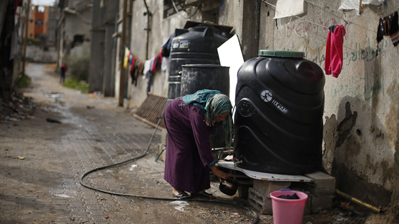 MIDEAST-PALESTINIANS/ISRAEL A Palestinian woman fills a kettle with water from a tank placed outside her house, that witnesses said was damaged by Israeli shelling during the July-August war between Israel and Hamas-led Gaza militants, in the east of Gaza City January 4, 2015. REUTERS/Suhaib Salem (GAZA - Tags: POLITICS CIVIL UNREST) - RTR4K04H