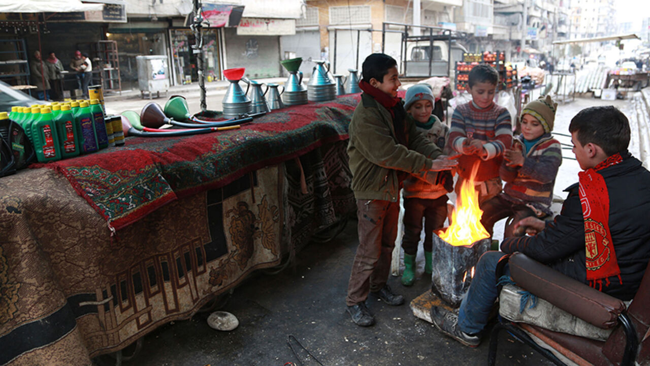 SYRIA-CRISIS/WIDERIMAGE Children warm themselves next to an open fire beside fuel barrels, engine oil and accessories displayed for sale in Aleppo January 13, 2015. Residents of Kafr Hamra, a town in the rural Aleppo countryside, refine crude oil in makeshift cottage refineries in warehouses and backyards for heating, operating bakeries and even running cars, just like most locals across rebel-held areas of Syria. The state no longer pumps gasoline to areas in rebel hands, and civilians have resorted to buying crude oil from armed