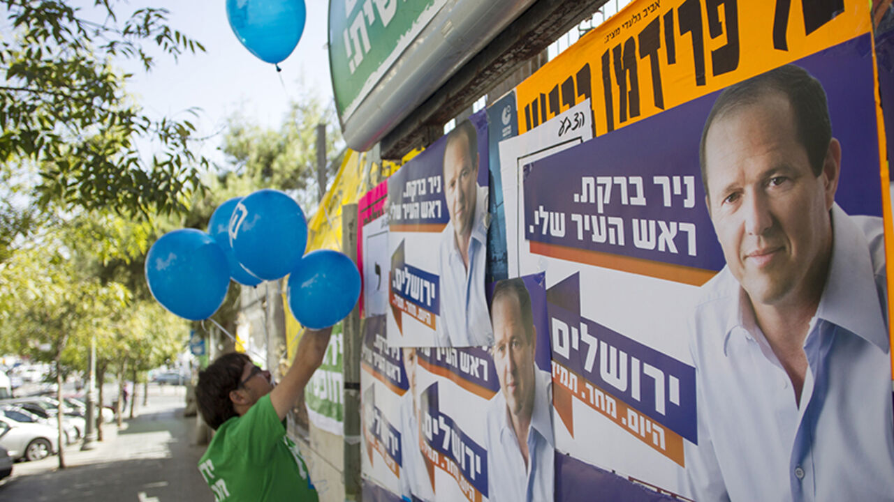 ISRAEL/ A supporter of the left wing Meretz party campaigning for municipal elections hangs balloons next to campaign posters of Jerusalem Mayor Nir Barkat in Jerusalem October 22, 2013. REUTERS/Baz Ratner (JERUSALEM - Tags: POLITICS ELECTIONS) - RTX14JPY