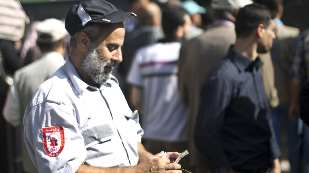 Nic6382138 A Palestinian employee of the former Hamas government counts his money outside a post office in Gaza City on October 29, 2014 after receiving 1,200 US dollars which is part of his wages that has been delayed for months. The Palestinian national unity government headed by prime minister Rami Hamdallah sent the previous day roughly 30 million dollars by car across the Erez border crossing from the West Bank to the Gaza Strip to pay 24,000 former employees. AFP PHOTO / MAHMUD HAMS (Photo credit should r