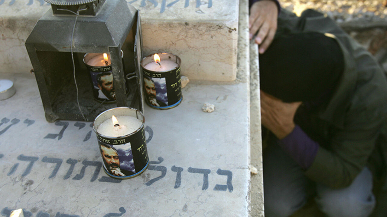 DV124296 JERUSALEM, : Candles burn with the image of the late Brooklyn born Rabbi Meir Kahane as a follower prays at his grave at the Givat Shaul cemetery on the outskirts of Jerusalem 09 November 2006, to mark the 16th anniversary of his assassination by an Arab gunman in Manhattan. The anti-Arab Jewish militant movement founded by Kahane has in the past claimed responsibility for dozens of shootings of Palestinians in the West Bank, including the notorious 1994 massacre of 29 worshippers at a Hebron Mosque. AFP