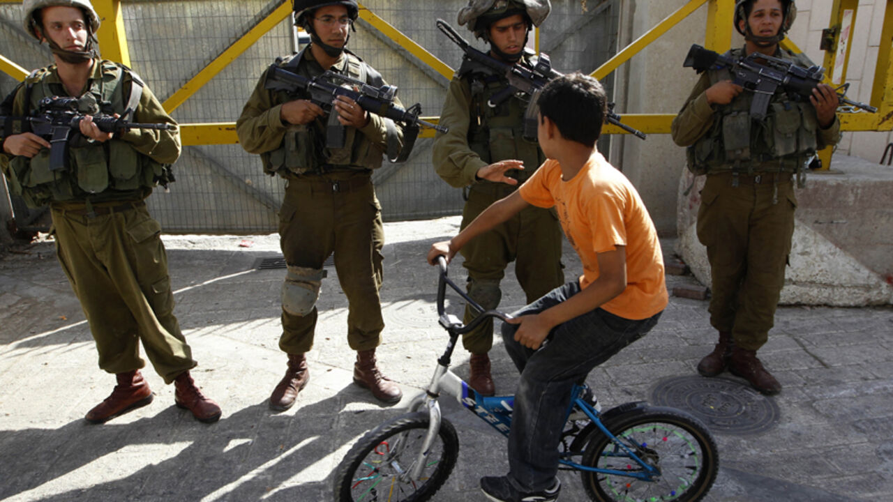PALESTINIANS-ISRAEL/ A Palestinian boy rides his bicycle past Israeli soldiers during a protest, by both Palestinian and foreign activists against the continued closure of Shuhada street to Palestinians, in the West Bank city of Hebron August 7, 2010. REUTERS/Ammar Awad (WEST BANK - Tags: CIVIL UNREST MILITARY IMAGES OF THE DAY) - RTR2H4DA