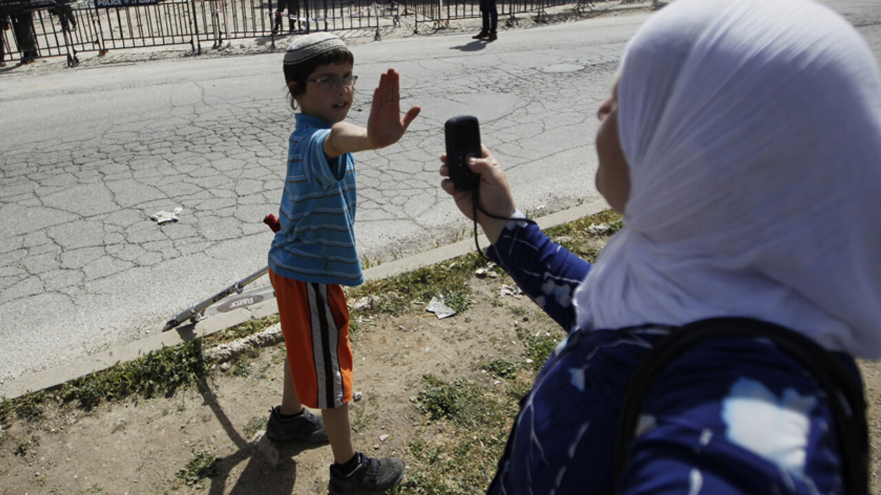 PALESTINIANS-ISRAEL/SETTLERS A Jewish boy lifts his hand to prevent a Palestinian from taking his picture near a police barrier cordoning off a building the day after Israeli police evicted Jewish settlers who occupied it in the West Bank city of Hebron April 5, 2012. Israeli police evicted Jewish settlers on Wednesday from the building they said they had bought from a Palestinian in the heart of Hebron, a frequent flashpoint in the Israeli-Palestinian conflict. REUTERS/Ammar Awad (WEST BANK - Tags: POLITICS MILITARY CIVIL UNREST) - RT