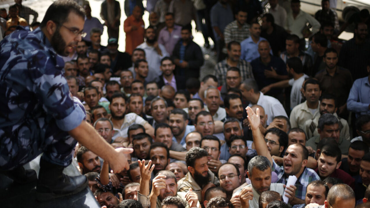 MIDEAST-PALESTINIANS/UNITY A Palestinian policeman gestures as Hamas-hired civil servants wait to receive a payment in Gaza City October 29, 2014. Some 24,000 civil servants hired by the Islamist group Hamas, many of whom have not received a full salary in almost a year, finally got some pay on Wednesday from the new Palestinian unity government based in the West Bank. The funds were supplied by the gas-rich kingdom of Qatar, which is an ally of Hamas. But the fact the cash was delivered by the West Bank administration gave a boost t