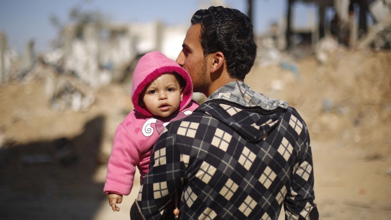 Nic6422074 A Palestinian man carries his child on February 26, 2015 in Gaza City's al-Shejaiya neighbourhood next to buildings destroyed during the 50-day war between Israel and Hamas militants in the summer of 2014. More than 100,000 homes in the Gaza Strip were damaged or destroyed in Israeli bombardment during the 50-day conflict. AFP PHOTO / MOHAMMED ABED (Photo credit should read MOHAMMED ABED/AFP/Getty Images)
