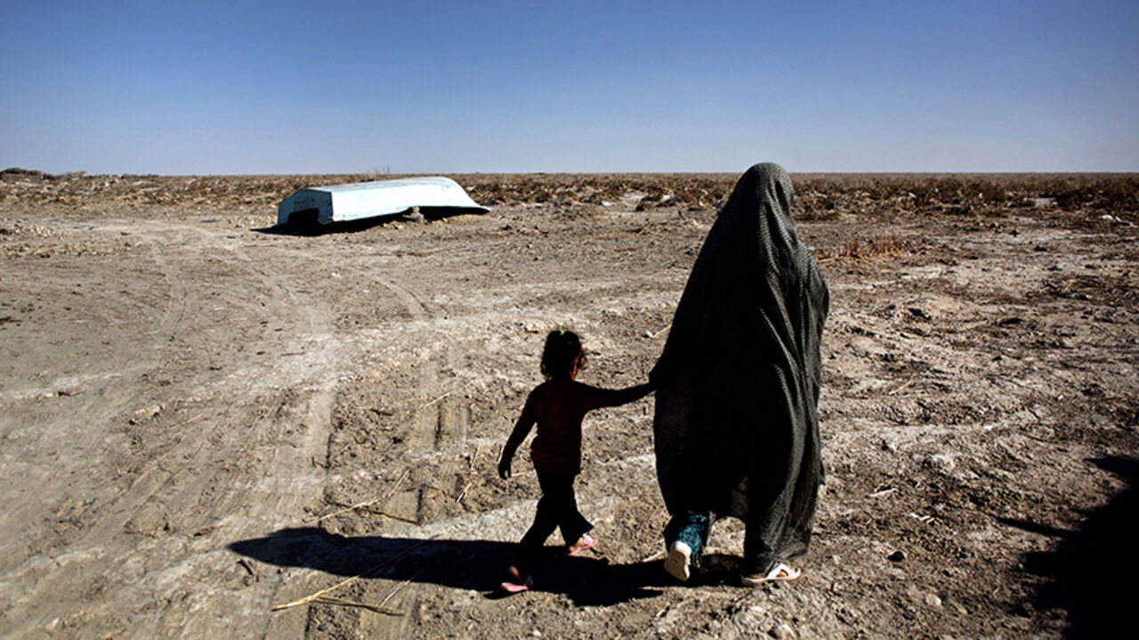 Nic6413565 An Iranian woman walks with her daughter past an abandoned boat in Sikh Sar village at Hamoon wetland near the Zabol town, in southeastern province of Sistan-Baluchistan bordering Afghanistan on February 2, 2015. AFP PHOTO/BEHROUZ MEHRI (Photo credit should read BEHROUZ MEHRI/AFP/Getty Images)