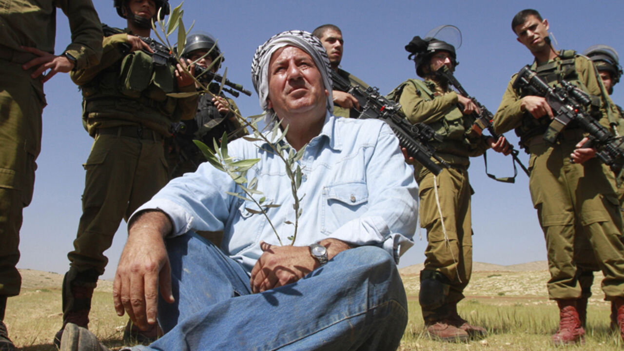 Israeli soldiers stand guard as a Palestinian farmer sits on the ground after planting olive trees during a protest against what Palestinians say is land confiscation for Jewish settlements in the Jordan Valley, a hotly contested part of the occupied West Bank April 8, 2014. REUTERS/Abed Omar Qusini (WEST BANK - Tags: POLITICS AGRICULTURE MILITARY) - RTR3KEMR