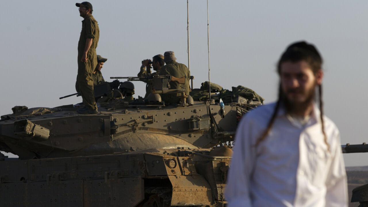 MIDEAST-GAZA/ An ultra-Orthodox Jewish man walks near Israeli army tanks near the border with Gaza July 30, 2014. Israeli fire killed at least 43 Palestinians in the Gaza Strip early on Wednesday as the Jewish state said it targeted Islamist militants at dozens of sites across the coastal enclave, while Egyptian mediators prepared a revised ceasefire proposal. REUTERS/Siegfried Modola (ISRAEL - Tags: CIVIL UNREST MILITARY CONFLICT RELIGION POLITICS) - RTR40LLQ