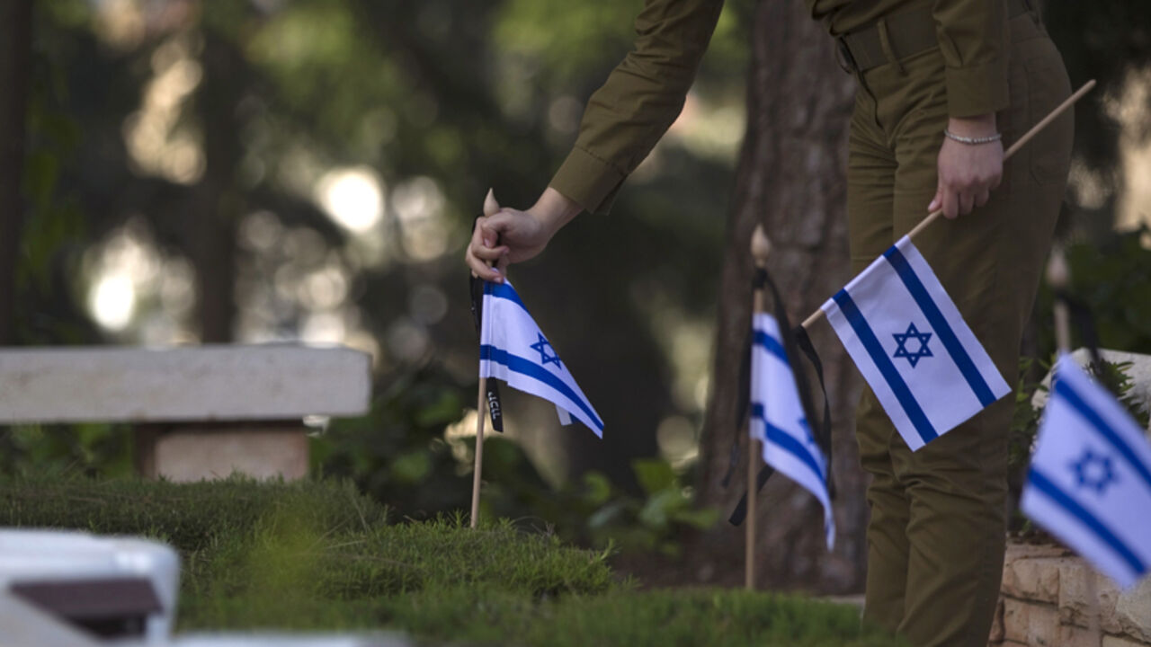 ISRAEL-MEMORIAL/ An Israeli soldier places flags on graves of fallen soldiers during a ceremony at the Mount Herzl military cemetery in Jerusalem, ahead of Memorial Day April 19, 2015. Israel commemorates its fallen soldiers on Memorial Day, which begins Tuesday night. REUTERS/Ronen Zvulun - RTR4XX69