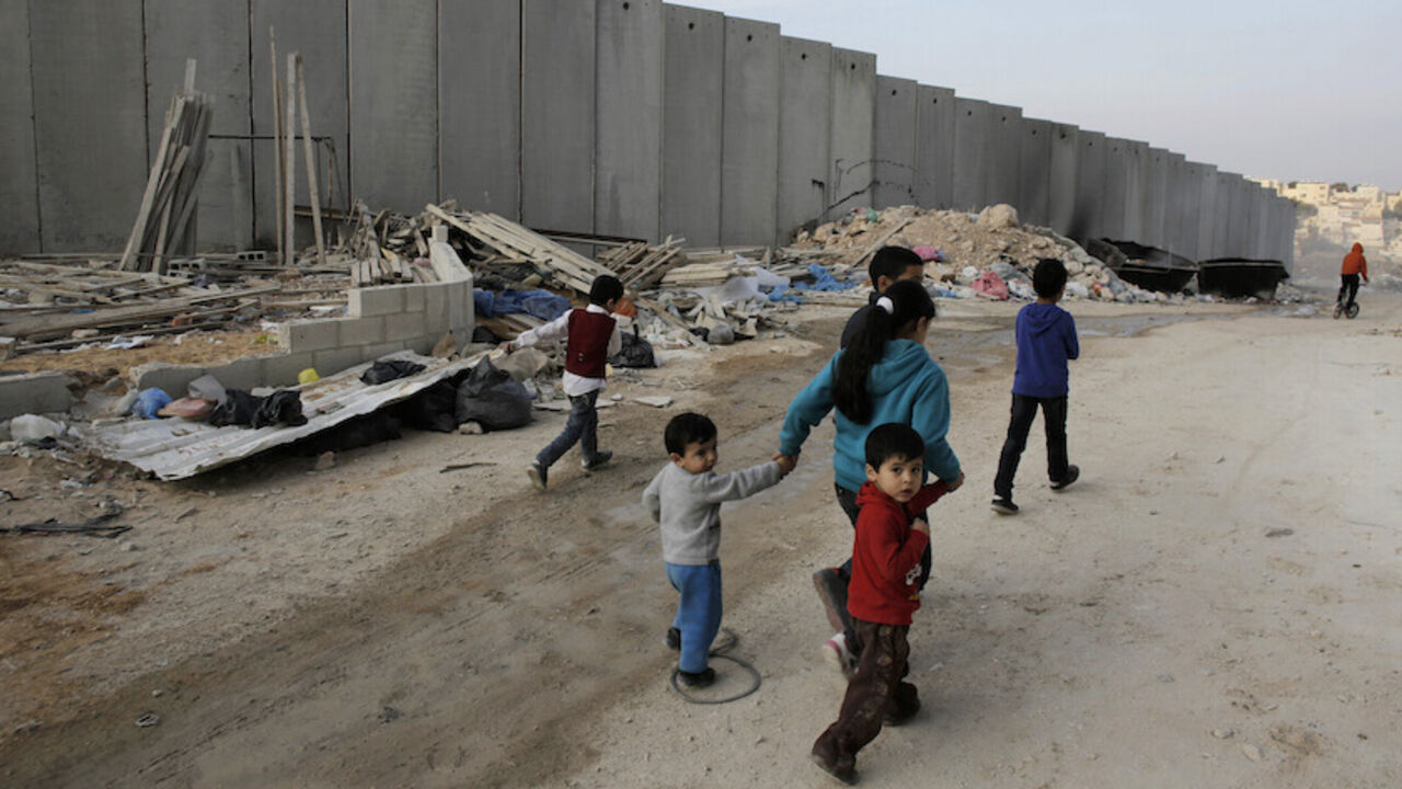 ISRAEL-PALESTINIANS/JERUSALEM Palestinian children walk past garbage discarded near a section of the controversial Israeli barrier, in Shuafat refugee camp in the West Bank near Jerusalem November 21, 2013. Marooned behind the wall, Israel's controversial barrier, the Shuafat refugee camp reveals the state's uneven treatment of Arab and Jewish neighbourhoods, creating a de facto partition of Jerusalem, which is the epicentre of the Middle East conflict. Picture taken November 21, 2013. REUTERS/Ammar Awad (WEST BANK - Tags: POLITICS SOCI