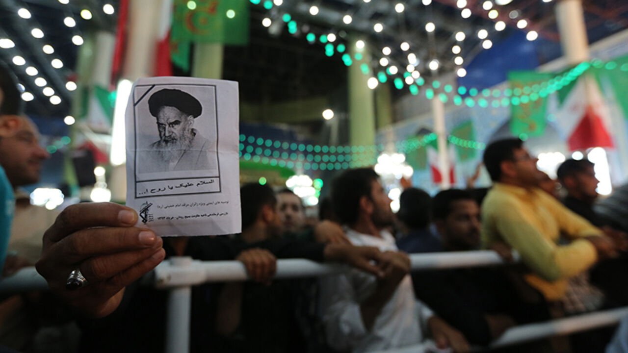 Par7897325 An Iranian man holds a photo of late Ayatollah Ruhollah Khomeini, while listening to Iran's President Hassan Rouhani delivering a speech on the eve of the 25th anniversary of the death of Islamic revolutionary leader Khomeini, at Khomeini's mausoleum in a suburb of Tehran on June 3, 2014. AFP PHOTO / ATTA KENARE (Photo credit should read ATTA KENARE/AFP/Getty Images)