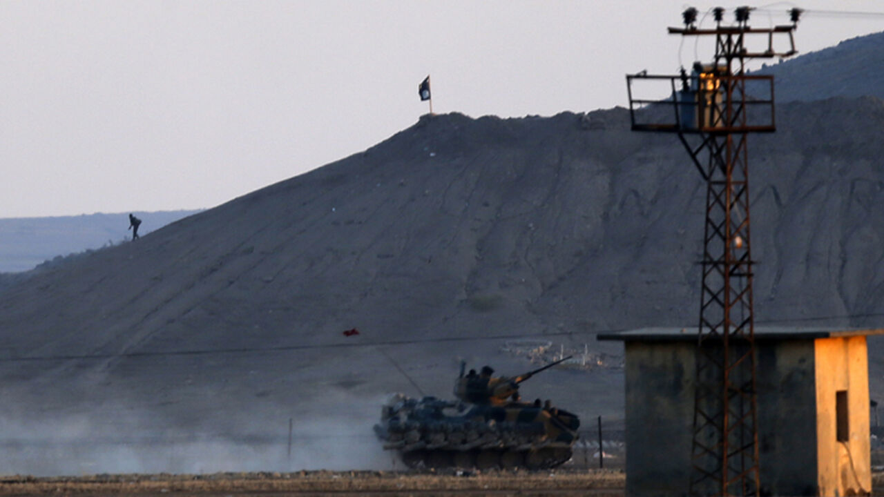 MIDEAST-CRISIS/TURKEY An Islamic State fighter walks near a black flag belonging to the Islamic State as a Turkish army vehicle takes position near the Syrian town of Kobani, as pictured from the Turkish-Syrian border near the southeastern town of Suruc, Sanliurfa province October 7, 2014. Turkey has asked the United States to step up air strikes to keep Islamic State militants from seizing a key Syrian Kurdish border town, a senior Turkish official was quoted as saying on Tuesday. Islamic State fighters advancing into the south