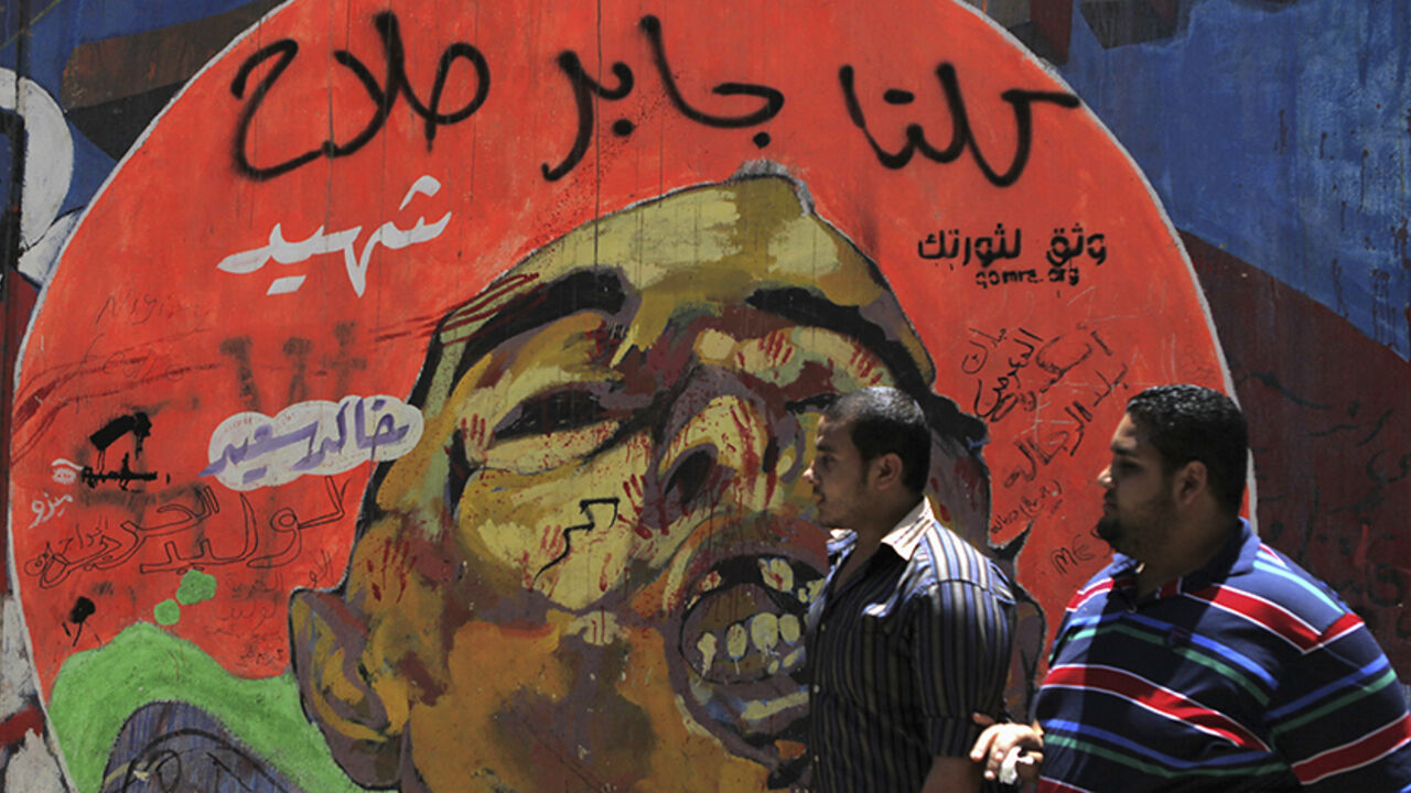 EGYPT People walk in front of a graffiti of activist Khaled Said on the wall near Tahrir Square in downtown Cairo on the third anniversary of Said's death, June 6, 2013. Said, 28, was beaten to death by police in Alexandria in June 2010 with his body barely recognisable after he posted a video showing police officers sharing the spoils of a drugs bust, according to his family. The act of brutality galvanised further protests, in particular, the anti-torture Facebook page "We are Khaled Said". The page helped crys